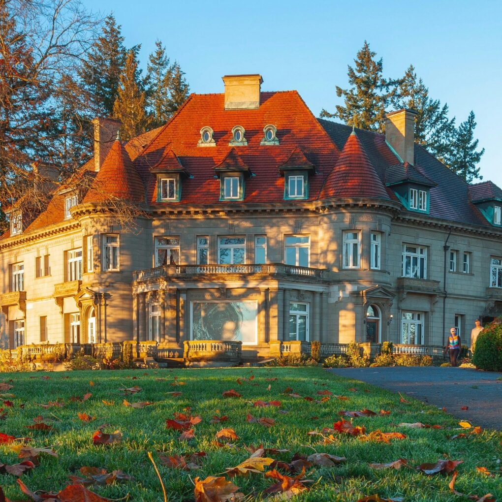 A mansion with a dark orange roof, in an autumnal setting.