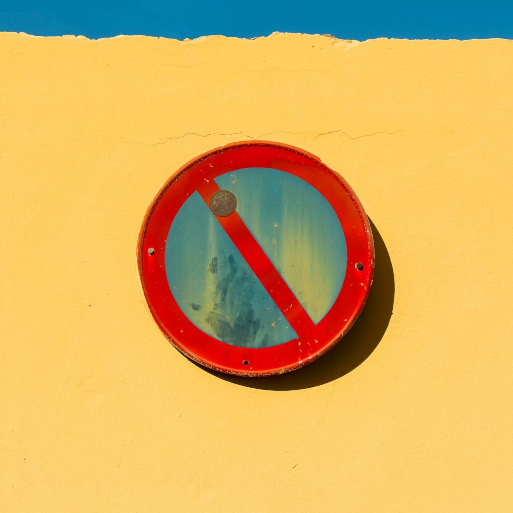 A no parking sign mounted on a bright yellow wall under a clear blue sky