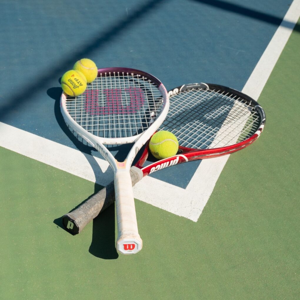 Two tennis rackets and balls on a sunlit court.