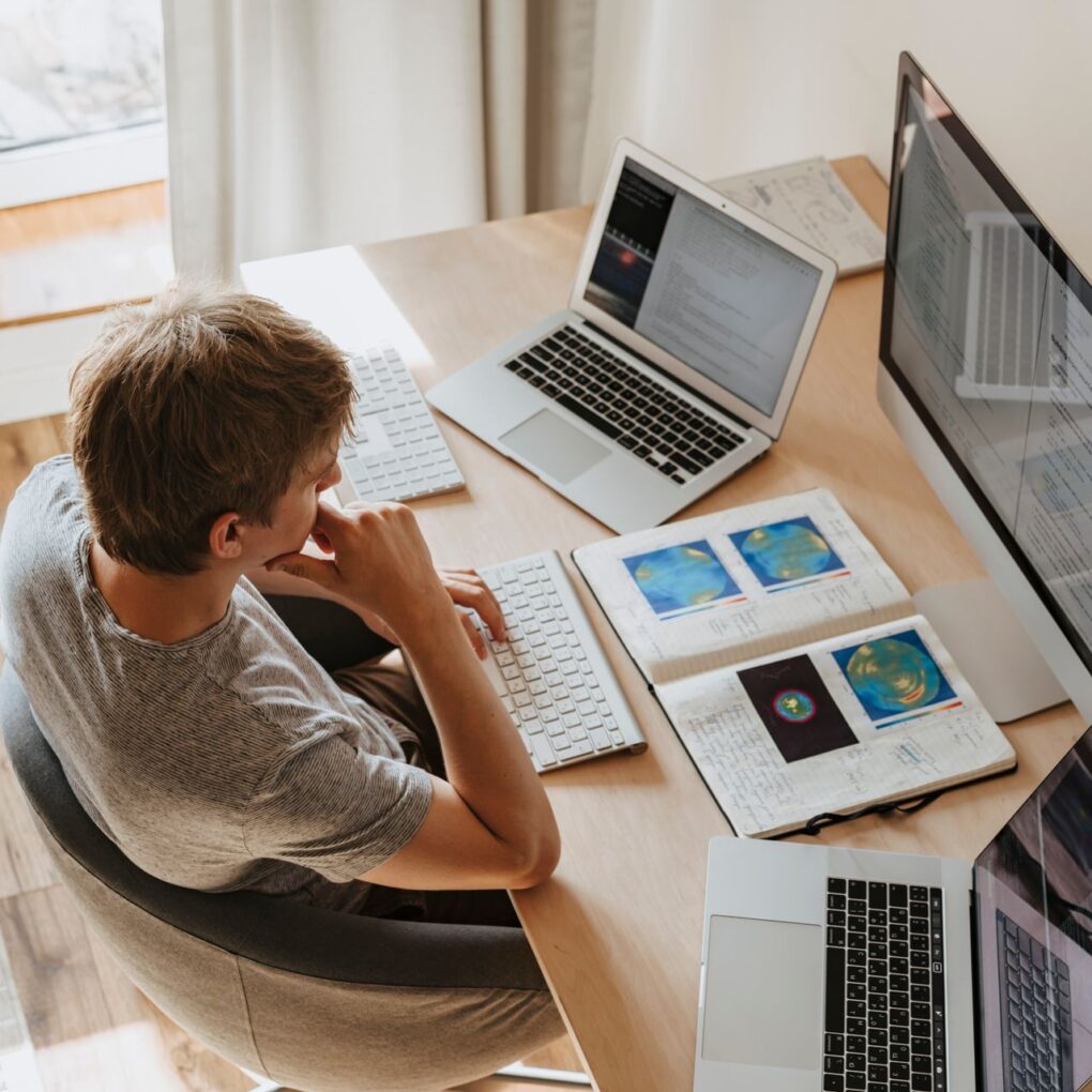 Top view of a young man working on multiple laptops in a home office.
