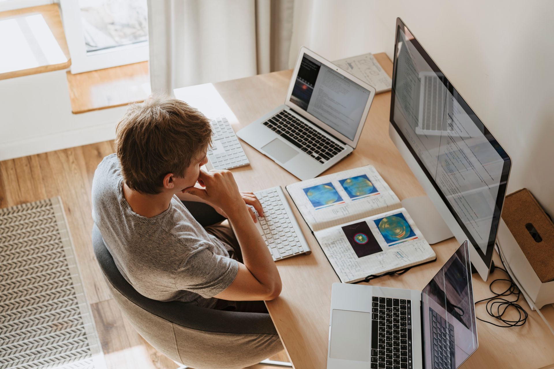 Top view of a young man working on multiple laptops in a home office.