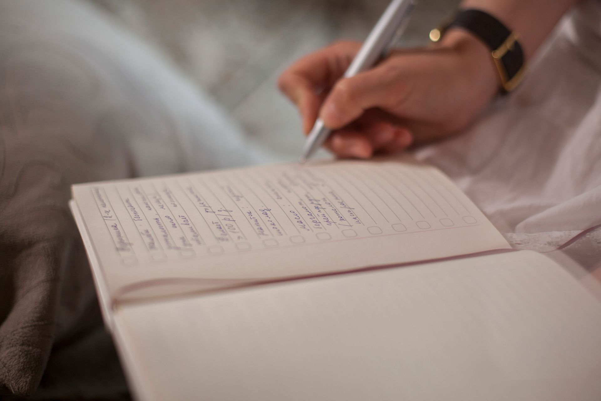 Close-up of a person writing in a lined notebook with a silver pen, creating a handwritten checklist.